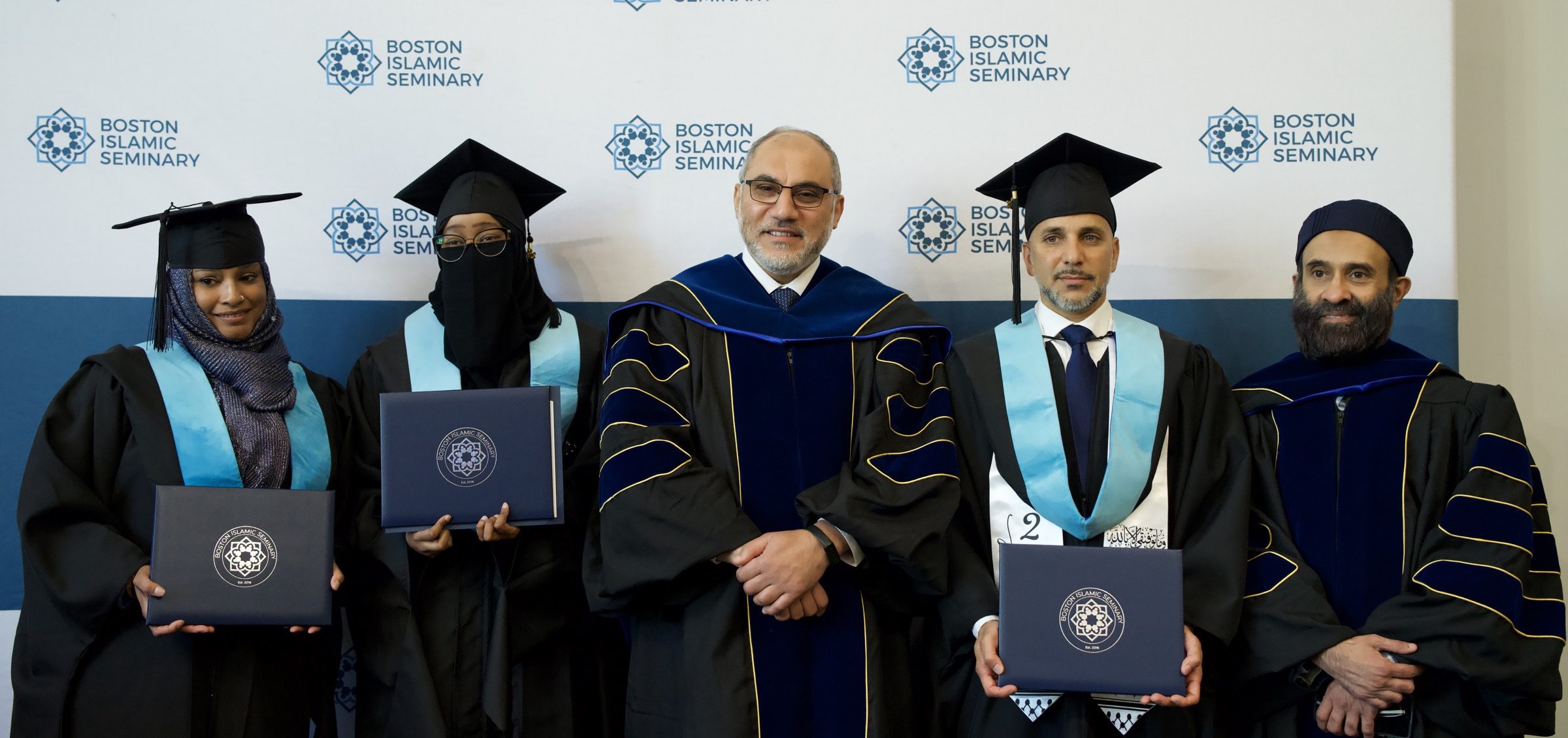 Three BIS graduates with seminary leadership at the 2026 graduation, holding closed diploma covers.
